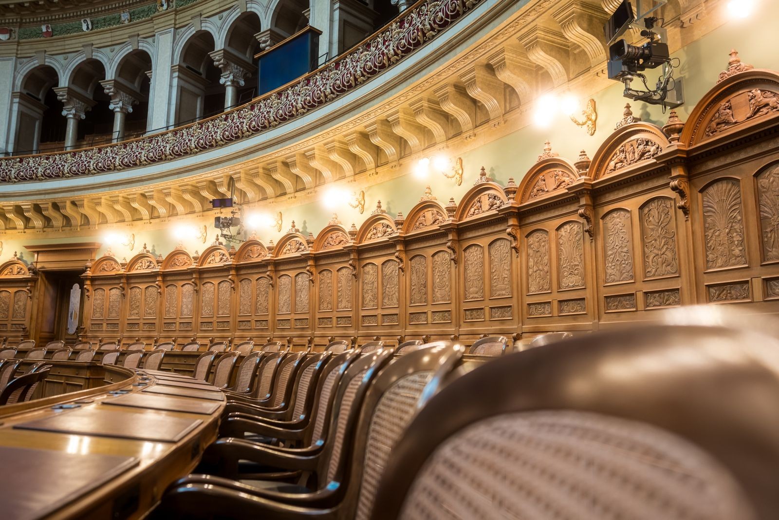 Grand government council chamber with tiered seating, ornate wooden balconies, and a glass dome ceiling